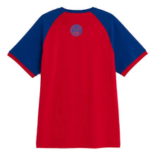 A red and blue raglan t-shirt shown from the back, featuring a blue circular crest graphic on the upper back. The t-shirt has a solid red body and blue sleeves with red trim, photographed against a light gray background.