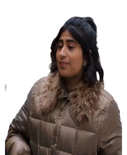 A woman wearing a beige puffer jacket with a brown faux-fur collar, standing in a crowd at an outdoor protest with signs in the background.