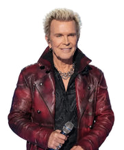 A man with platinum blonde hair wearing a distressed red leather jacket over a black shirt, holding a microphone on a stage with a blue and white lit background.