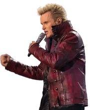 A male performer on stage wearing a glossy dark red leather jacket and holding a microphone, with a blurred stage background.