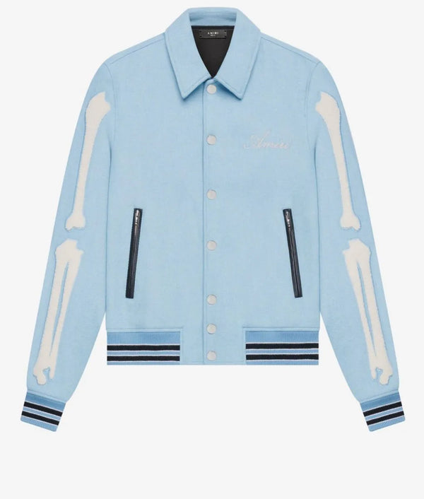 A light blue denim jacket featuring bone appliques on the sleeves, black zipper details, and striped ribbed cuffs and hem, shown against a plain white background.