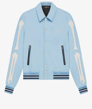 A light blue denim jacket featuring bone appliques on the sleeves, black zipper details, and striped ribbed cuffs and hem, shown against a plain white background.