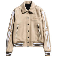 A beige varsity-style jacket with white bone appliques on the sleeves, striped ribbed cuffs and hem, and a black button front, shown on a light gray background.