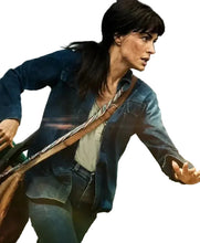A woman in a blue denim jacket and jeans carrying a large brown leather bag across her body, captured in a dynamic action pose against a blurred outdoor background.