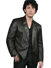 A man wearing a black leather blazer over a black shirt and black pants, standing against a plain white background.