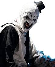 A person wearing a creepy clown mask costume with a white face covering, black painted eyes and mouth details, a black top hat, and a black-and-white outfit, posed in a dim blue-lit industrial setting.