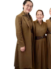 Three women wearing matching brown uniform-style coats and dresses against a plain white background.