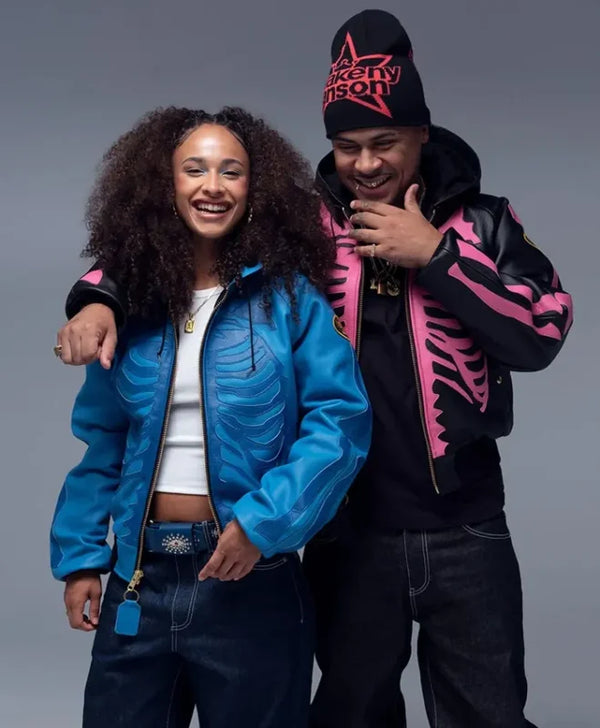 A man and a woman posing together in streetwear. The woman wears a bright blue ribbed bomber jacket over a white crop top and dark jeans.