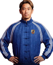 A man wearing a royal blue traditional Chinese-style jacket with white stripes on the sleeves, posed against a solid red background.