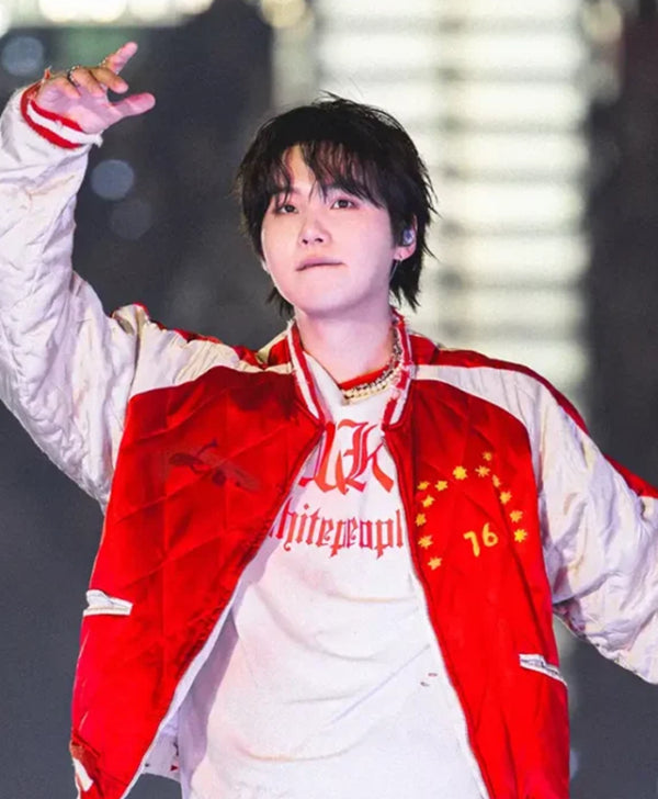A person wearing a red and white varsity-style jacket over a white graphic T-shirt, posing with one arm raised in a performance or stage setting.