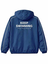 A blue hooded windbreaker jacket shown from the back, featuring the words 'KEEP SWIMMING' and a small wave graphic printed in white across the upper back. The jacket has white piping along the shoulders and sleeves.