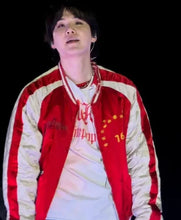 A man wearing a red and cream varsity-style jacket over a white t-shirt, photographed against a solid black background.