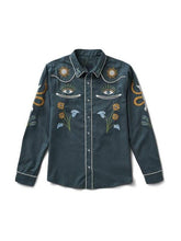 A dark teal button-up shirt with intricate embroidered designs including eyes, flowers, suns, and snakes, accented with white piping, shown against a plain white background.
