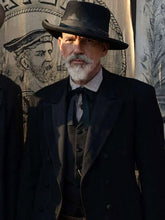 A man wearing a black wide-brimmed hat, black double-breasted suit jacket, dark vest, and black bow tie, standing in front of a vintage illustrated backdrop.