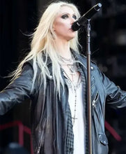 A blonde woman on stage wearing a black leather jacket over a white shirt and layered necklaces, singing into a microphone.