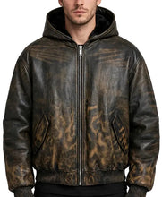 A man wearing a distressed brown leather hooded jacket with a front zipper, ribbed knit collar, cuffs, and hem, shown against a plain gray studio background.