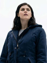 A woman with dark hair looking upward, wearing a dark navy hooded jacket over a light gray top, set against a bright white sky.
