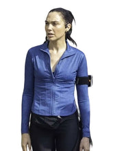 A woman wearing a fitted blue long-sleeve athletic zip-up top with a front zipper and ruched bust, paired with black leggings and a black armband phone holder, against a plain white background.