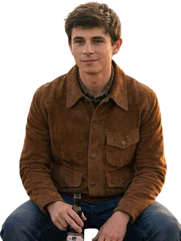 A man wearing a brown suede jacket over a dark shirt and blue jeans, holding a bottle and a glass against a plain white background.