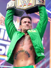 A shirtless man with tattoos holds a large WWE championship belt above his head while wearing an open bright green jacket and matching green trunks in a wrestling event setting.