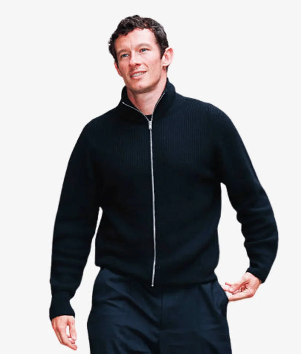 A man wearing a black ribbed zip-up sweater with a stand collar and matching dark trousers, photographed against a plain light gray background.