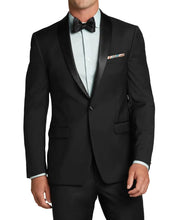 A man wearing a black tuxedo jacket with black satin shawl lapels, a black bow tie, a light blue dress shirt, and a multicolor patterned pocket square, shown against a solid gray background.