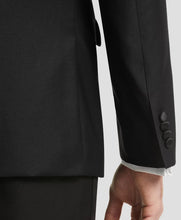 Close-up of a black tailored jacket sleeve with three buttons and a white shirt cuff visible at the cuff placket, shown against a light gray studio background.