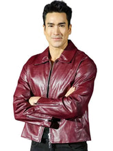 A man wearing a shiny burgundy leather jacket with a high collar and front zipper, posed with arms crossed against a plain white background.