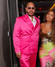 A man wearing a bright hot pink double-breasted suit with a white shirt and sunglasses, standing in a dimly lit indoor setting.