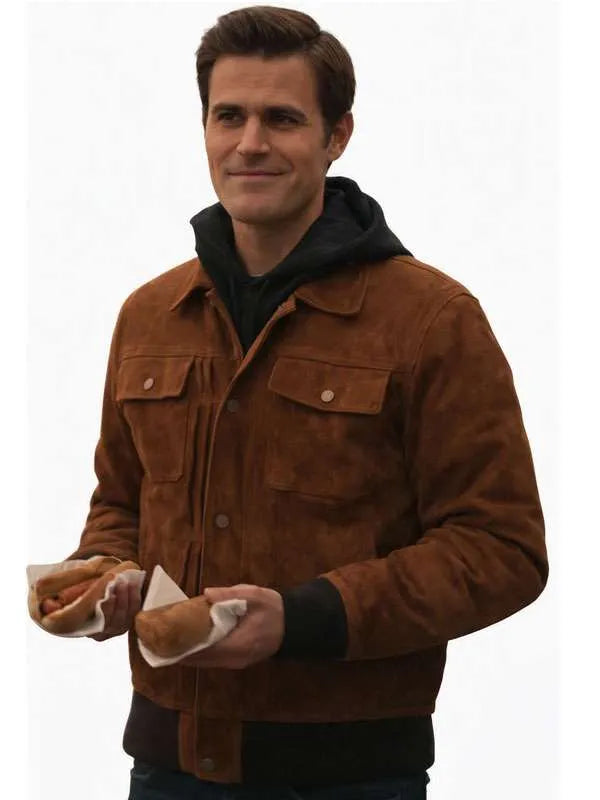 A man wearing a brown suede jacket over a black hoodie, holding two hot dogs against a plain white background.