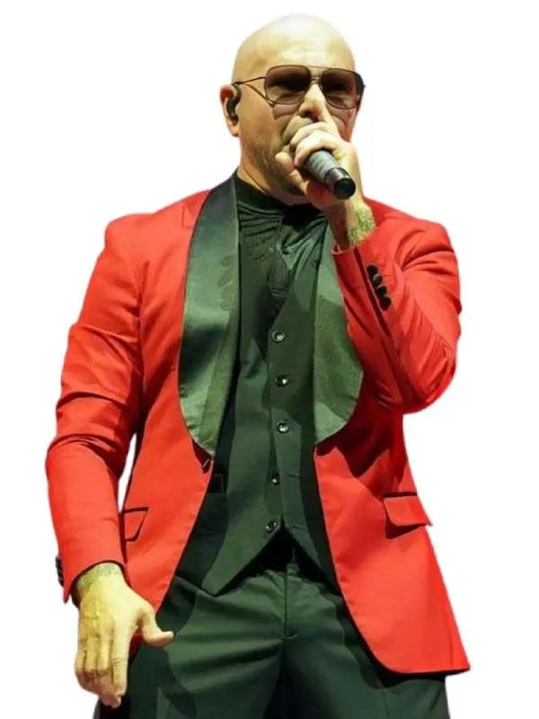 A bald man wearing a bright red blazer over a dark green shirt and vest, holding a microphone while performing on stage against a plain white background.