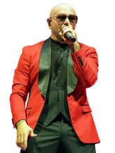 A bald man wearing a bright red blazer over a dark green shirt and vest, holding a microphone while performing on stage against a plain white background.