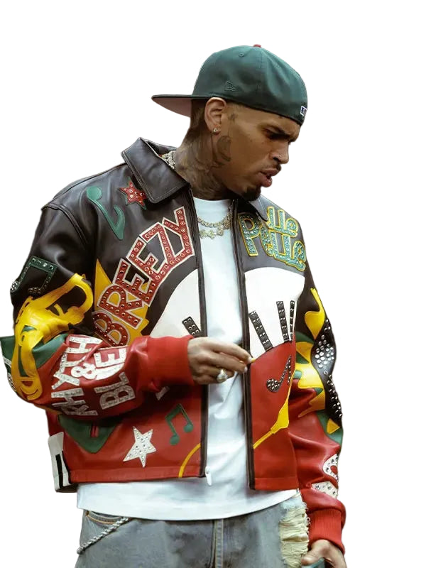 A man wearing a colorful, heavily decorated leather jacket with 'Breez' and 'Pimp' graphics, a green baseball cap, and a white t-shirt, standing in an indoor setting.
