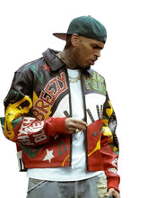 A man wearing a colorful, heavily decorated leather jacket with 'Breez' and 'Pimp' graphics, a green baseball cap, and a white t-shirt, standing in an indoor setting.