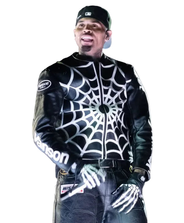 A man wearing a black leather jacket with a white spiderweb pattern on the front, black gloves, and a black baseball cap, standing in front of a blurred crowd.