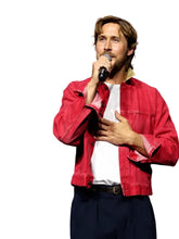 A man speaking at a Comic-Con event, wearing a red denim jacket over a white t-shirt and dark pants, holding a microphone.