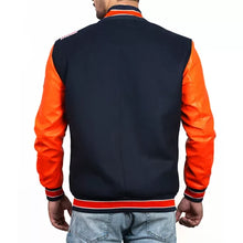 A man viewed from the back wearing a varsity-style jacket with a dark navy body and bright orange sleeves, paired with light blue jeans against a plain white background.