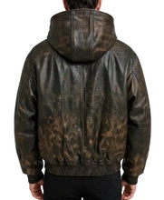 A person viewed from the back wearing a dark brown hooded jacket with a distressed, mottled brown-and-black leather-like finish. The jacket has a high hood, a central zipper, ribbed cuffs and hem, and black pants below it, photographed against a plain light gray studio background.
