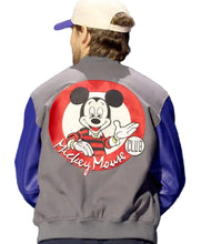 A person shown from behind wearing a gray and blue varsity-style jacket with a large Mickey Mouse graphic on the back, along with a white and blue cap.