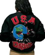 A person viewed from the back wearing a black varsity-style jacket with a large red 'USA' and 'DENIM JAYS' graphic, plus a black cat and blue globe patch on the back.