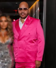 A man wearing a bright hot pink double-breasted satin suit with a white shirt and sunglasses, standing in a dimly lit indoor setting.
