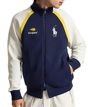 A person wearing a navy and white full-zip track jacket with yellow shoulder panels and logos, including a visible Polo Ralph Lauren pony logo and a US Open logo.
