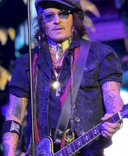 Johnny Cash on stage holding an electric guitar, wearing a black cap, sunglasses, layered necklaces, and a black denim vest over a pink shirt.