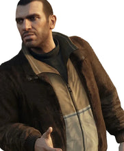 A man wearing a brown suede jacket over a beige and gray zip-up vest and dark turtleneck, standing outdoors in front of foliage and a lamp post.