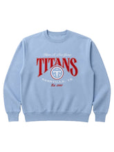 A light blue crewneck sweatshirt featuring a red and white graphic print on the front that reads 'TITANS NASHVILLE, TN' with a circular logo, displayed on a neutral light gray background.