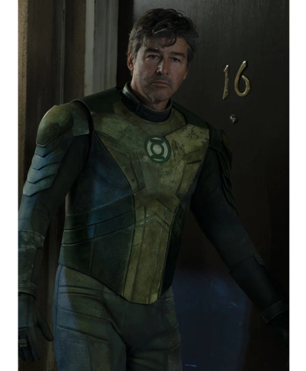 A man wearing a distressed green and black superhero costume with a glowing green emblem on the chest, standing in a dimly lit doorway next to a dark door marked with the number 16.