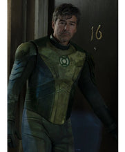 A man wearing a distressed green and black superhero costume with a glowing green emblem on the chest, standing in a dimly lit doorway next to a dark door marked with the number 16.