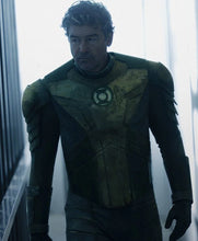 A man wearing a dark tactical suit with textured olive-green armor plating and a circular chest emblem, standing in a bright, hazy corridor.