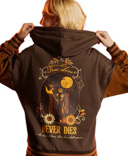 A person shown from behind wearing a dark brown hoodie with a large Halloween-themed graphic print on the back. The design features Jack Skellington, a cat, pumpkins, sunflowers, and the text 'True Love NEVER DIES'.