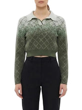 A model wearing a cropped, long-sleeve knit polo sweater with a green-to-gray gradient and a diamond argyle pattern, paired with black trousers, against a plain white background.